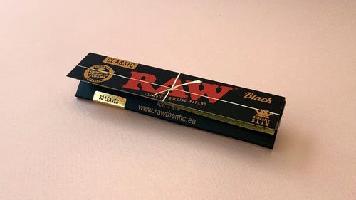 RAW Black - Classic King Size Slim, featuring ultra-thin, unbleached, and double-pressed artisan paper with a tan black and gold red themed packaging. RAW King Size Slim natural unrefined, 110x44mm, 32 leaves per booklet.