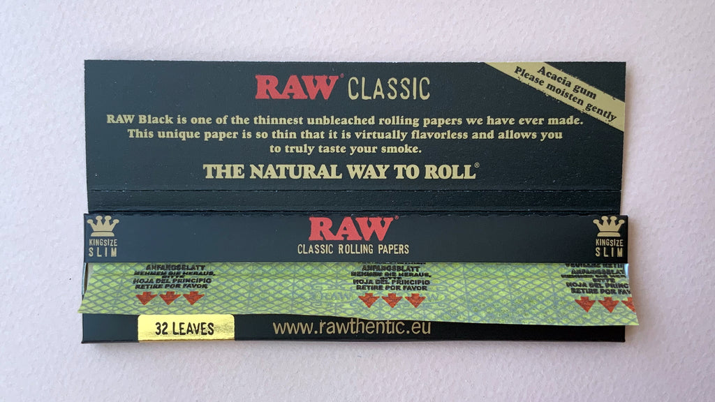 RAW Black - Classic King Size Slim, featuring ultra-thin, unbleached, and double-pressed artisan paper with a tan black and gold red themed packaging. RAW King Size Slim natural unrefined, 110x44mm, 32 leaves per booklet.