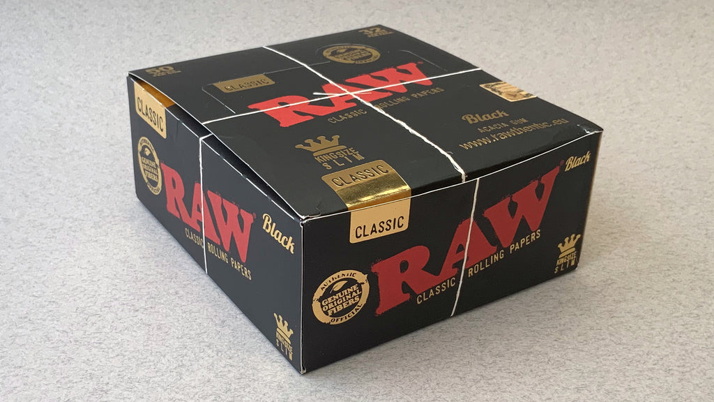 RAW Black - Classic King Size Slim, featuring ultra-thin, unbleached, and double-pressed artisan paper with a tan black and gold red themed packaging. RAW King Size Slim natural unrefined, 110x44mm, 32 leaves per booklet.