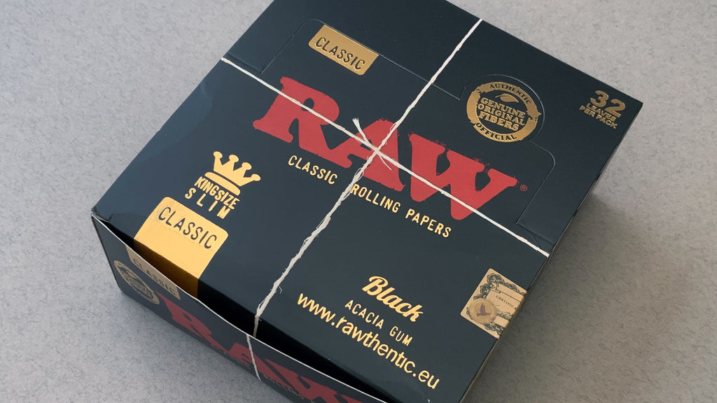 RAW Black - Classic King Size Slim, featuring ultra-thin, unbleached, and double-pressed artisan paper with a tan black and gold red themed packaging. RAW King Size Slim natural unrefined, 110x44mm, 32 leaves per booklet.