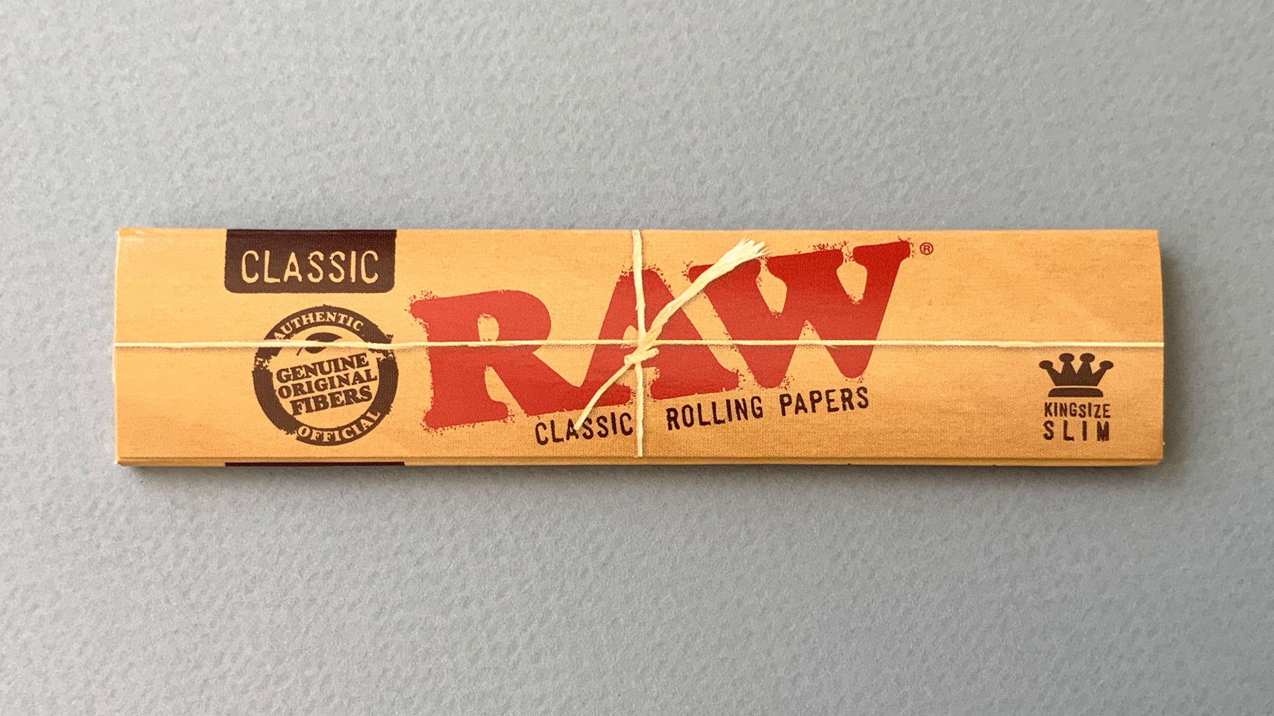 RAW Black - Classic King Size Slim, featuring ultra-thin, unbleached, and double-pressed artisan paper with a tan black and gold red themed packaging. RAW King Size Slim natural unrefined, 110x44mm, 32 leaves per booklet.