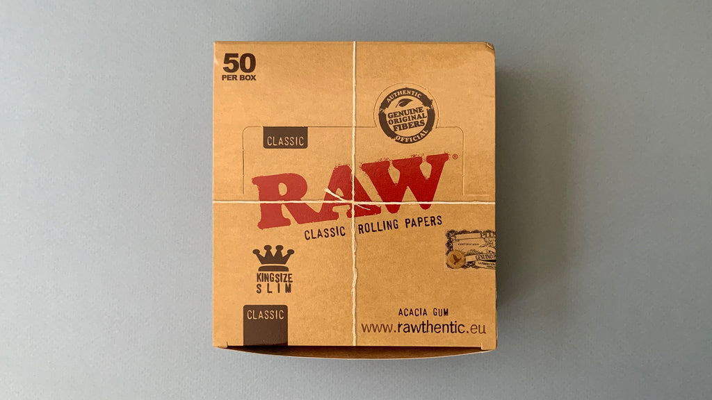 RAW Black - Classic King Size Slim, featuring ultra-thin, unbleached, and double-pressed artisan paper with a tan black and gold red themed packaging. RAW King Size Slim natural unrefined, 110x44mm, 32 leaves per booklet.
