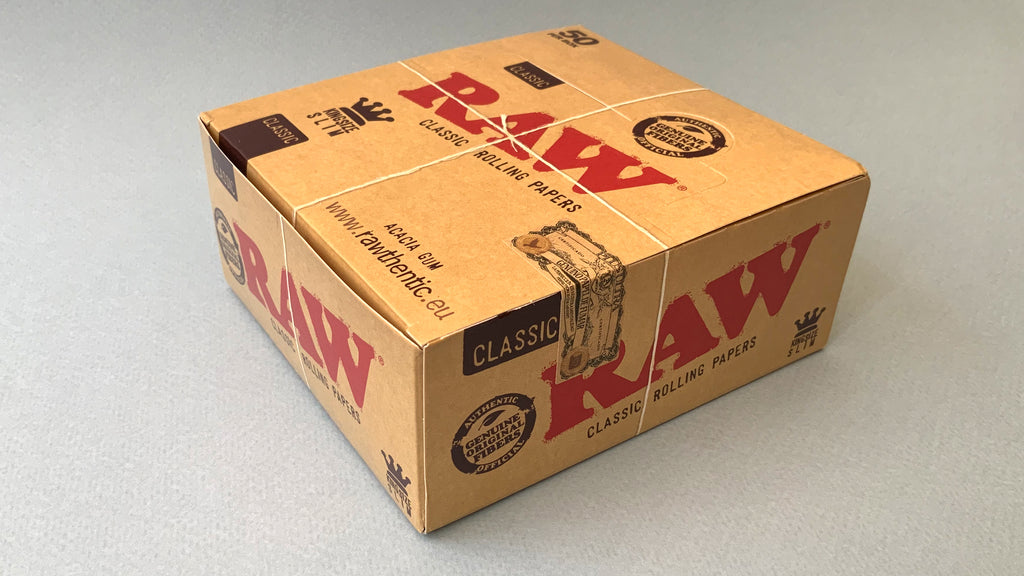 RAW Black - Classic King Size Slim, featuring ultra-thin, unbleached, and double-pressed artisan paper with a tan black and gold red themed packaging. RAW King Size Slim natural unrefined, 110x44mm, 32 leaves per booklet.