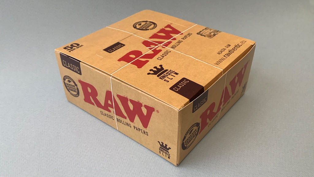 RAW Black - Classic King Size Slim, featuring ultra-thin, unbleached, and double-pressed artisan paper with a tan black and gold red themed packaging. RAW King Size Slim natural unrefined, 110x44mm, 32 leaves per booklet.